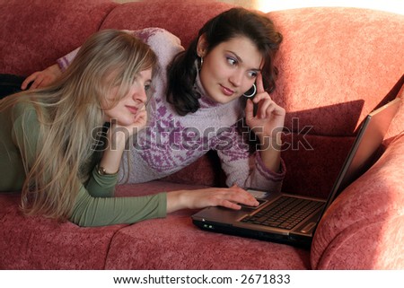 Two girl lie on a sofa and work on a notebook.