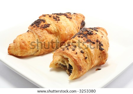 Two scrummy chocolate croissants on an off white plate, one has a bite taken from it.