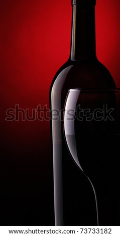Still life with bottle and glass of red wine on a dark red background.