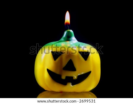 candle of yellow, green and black pumpkin ignited  in dark background reflected  on surface