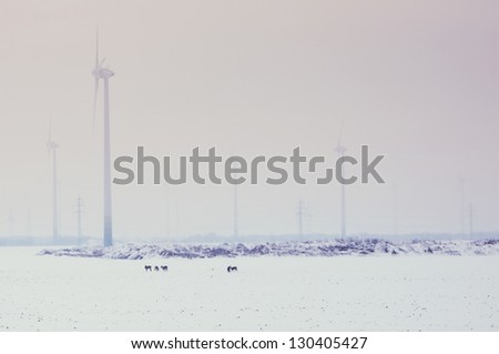 Moving wind turbine  in snow covered winter field and animals on the field