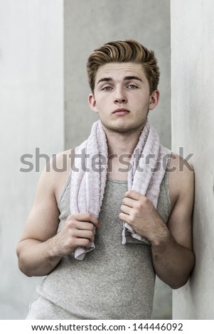 Young man with towel leans against concrete wall
