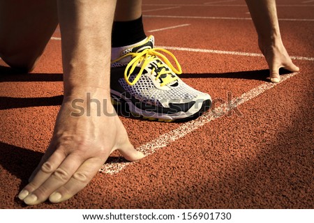 Runner In A Stadium Is In Start Position With Hands On The Line
