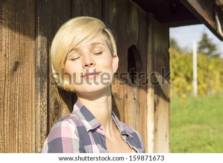Natural looking woman leans against the wall of  a hut and relaxes