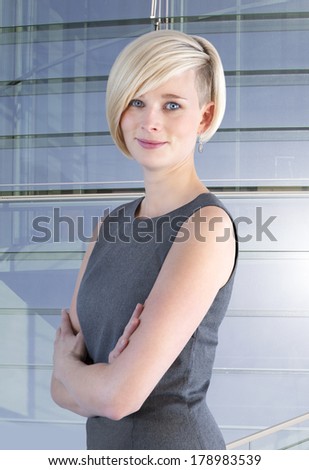 Young woman with crossed arms stands in front of a glass facade and smiles