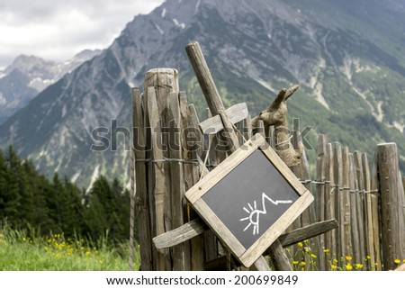 Wooden palisade with chalkboard hint panel in front of a mountain landscape. Chalkboard with empty space for own content