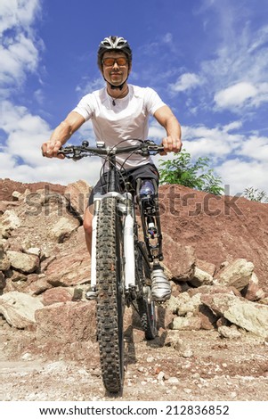 Shot of young male mountain bike rider with leg prosthesis between rocks.
