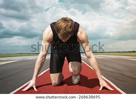Male version of airport runway starter. Runner in start position kneels with lowered head on a red tartan surface, ready to take of.