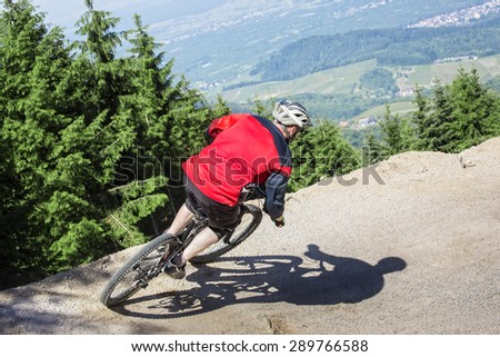 Mountain bike rider rides through a gravity slope of an artificial dirt track. The background shows the black forest in Germany.
