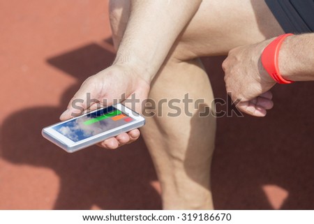 Sportsman man sits on a bench and checks his fitness statistic on a smartphone. He wears a fitness tracker wristband on his left arm.