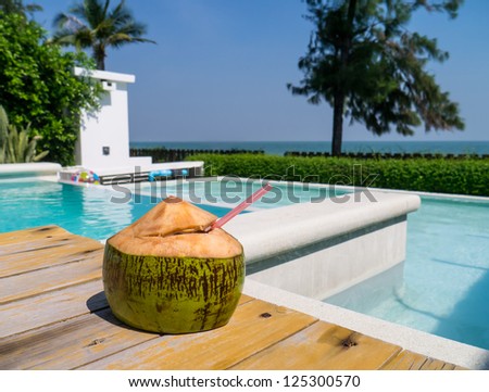 A fresh-cut coconut with drinking straw next to a pool in Thailand