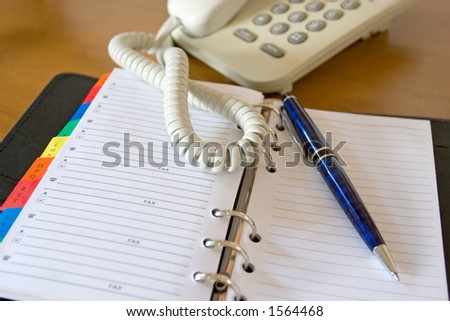 Close-up of a home phone, fine pen, and an open personal planner showing contacts pages