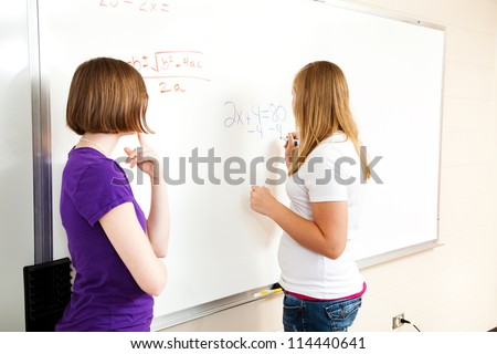 Two high school girls in algebra class, working equations on the board.