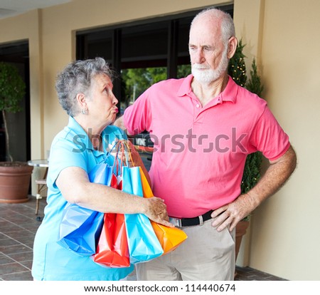 Senior woman addicted to shopping looks guilty as she explains to her husband.
