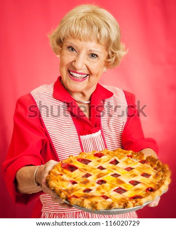 Sweet grandmother in vintage apron holding a delicious homemade cherry pie.
