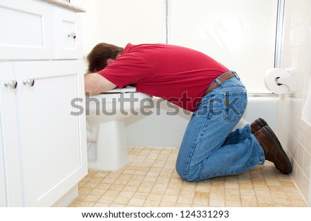 Man on his knees in the bathroom, vomiting into the toilet.