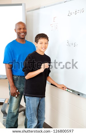 Handsome african-american teacher helps student at the board with math.