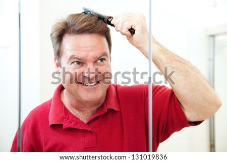 Handsome middle-aged man brushing his hair, looking in the bathroom mirror.