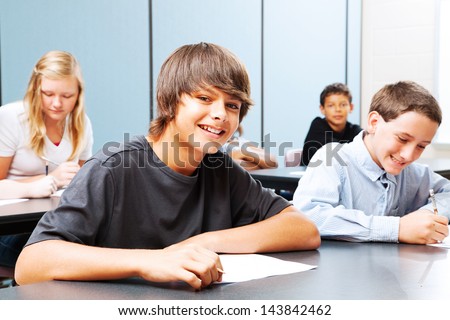 Class of teenagers in school, focus on suntanned boy in the front.