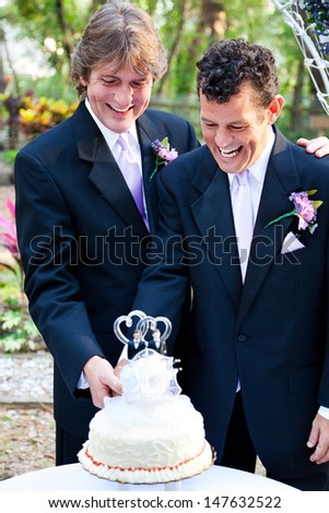 Two happy grooms cutting the cake at their wedding.