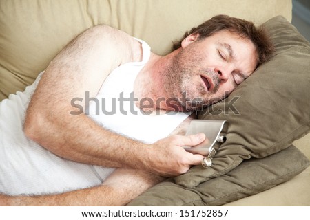 Unemployed man passed out drunk on the couch with a flask of booze in his hand.