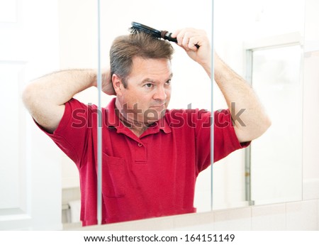 Handsome mature man in his bathroom brushing his hair in the mirror.