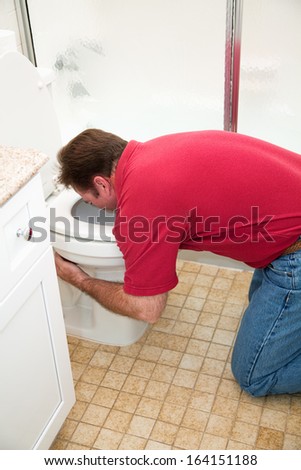 Man kneeling down in the bathroom, vomiting into the toilet.