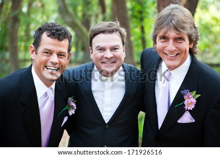 Minister posing with a handsome gay wedding couple he has just married.  *focus is on the minister.