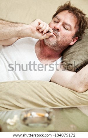 Middle aged man in his underwear getting high on his couch at home.