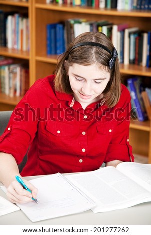 Teen girl doing research in library and taking notes.