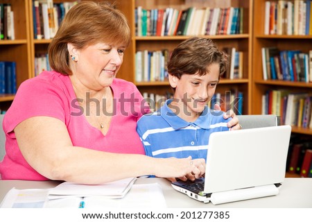 Mom or teacher working with a school boy on the computer in the library.