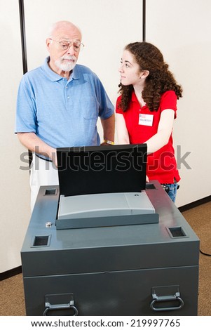 Young polling place volunteer helps a senior voter cast his ballot on new electronic equipment.
