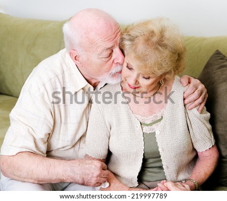 Elderly husband kissing his wife on the cheek in a gesture of consolation and love.