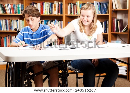 Teen boy and girl goofing around in the library.  The boy is disabled in a wheelchair.