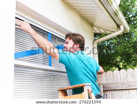 Man taping the windows on his home to protect from broken glass in a hurricane.