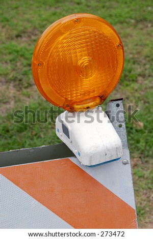 A closeup of an orange and white traffic barracade with the orange light on top. Grass in background.