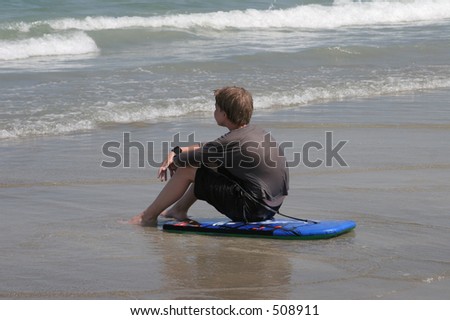 A boy sitting on his boogie board watching the tide roll in on the beach