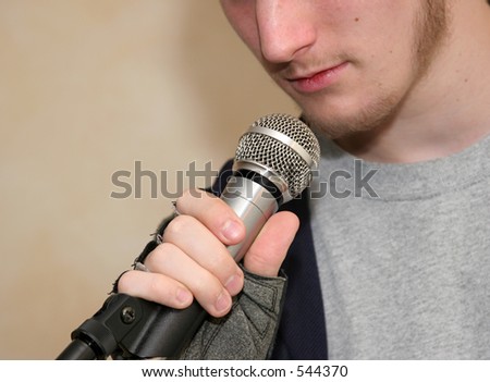 a closeup of a microphone with a man speaking into it (focus is on hand and microphone)