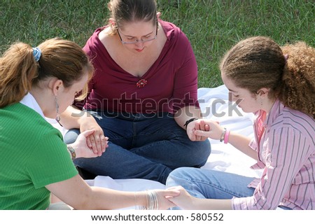 A group of teen girls having a prayer circle outdoors.