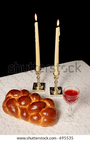 A table set for Shabbat with lighted candles, challah bread and wine. Vertical view with black background.