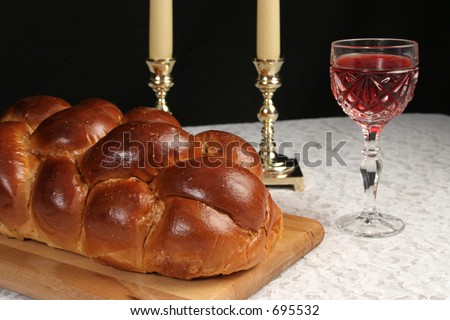 A table set for Shabbat with challah bread, candlesticks and wine.  Black background.