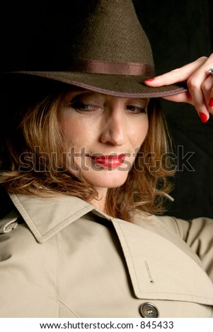 A beautiful woman in a trench-coat and fedora hat, looking behind her in a secretive way.