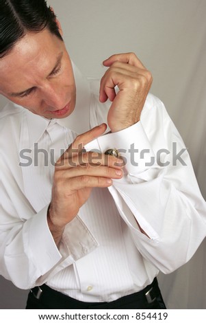 A handsome man putting on his cuff-links as he dresses in formal attire.
