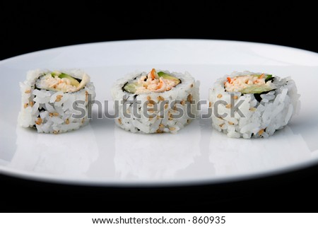 Three pieces of california roll on a white plate with black background.