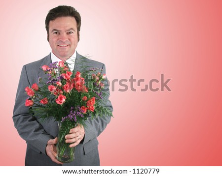 A handsome husband in a suit holding a bouquet of pink sweetheart roses over a pink packground.