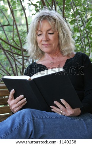 A beautiful mature woman relaxing and reading a book on her porch swing.