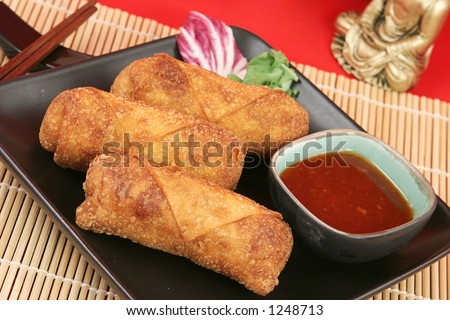 A plate of crispy fried egg rolls with spicy sweet chili sauce for dipping.