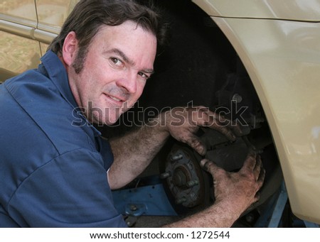 A handsome, friendly mechanic getting his hands dirty working on automotive brakes.