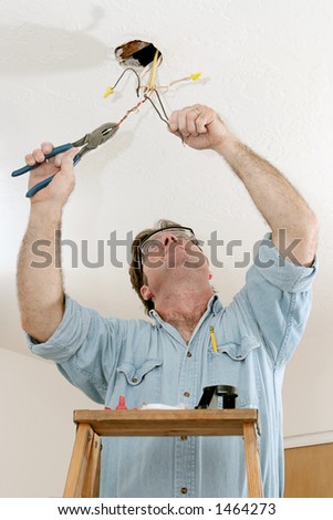 An electrician on a ladder using a pliers to separate wire.  Work is being done to code by a licensed master electrician.