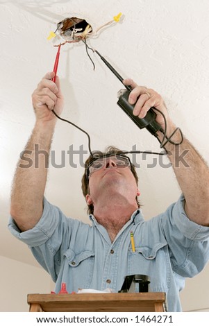 An electrician testing the voltage coming out of ceiling wires. Work is being performed to code by a licensed master electrician.